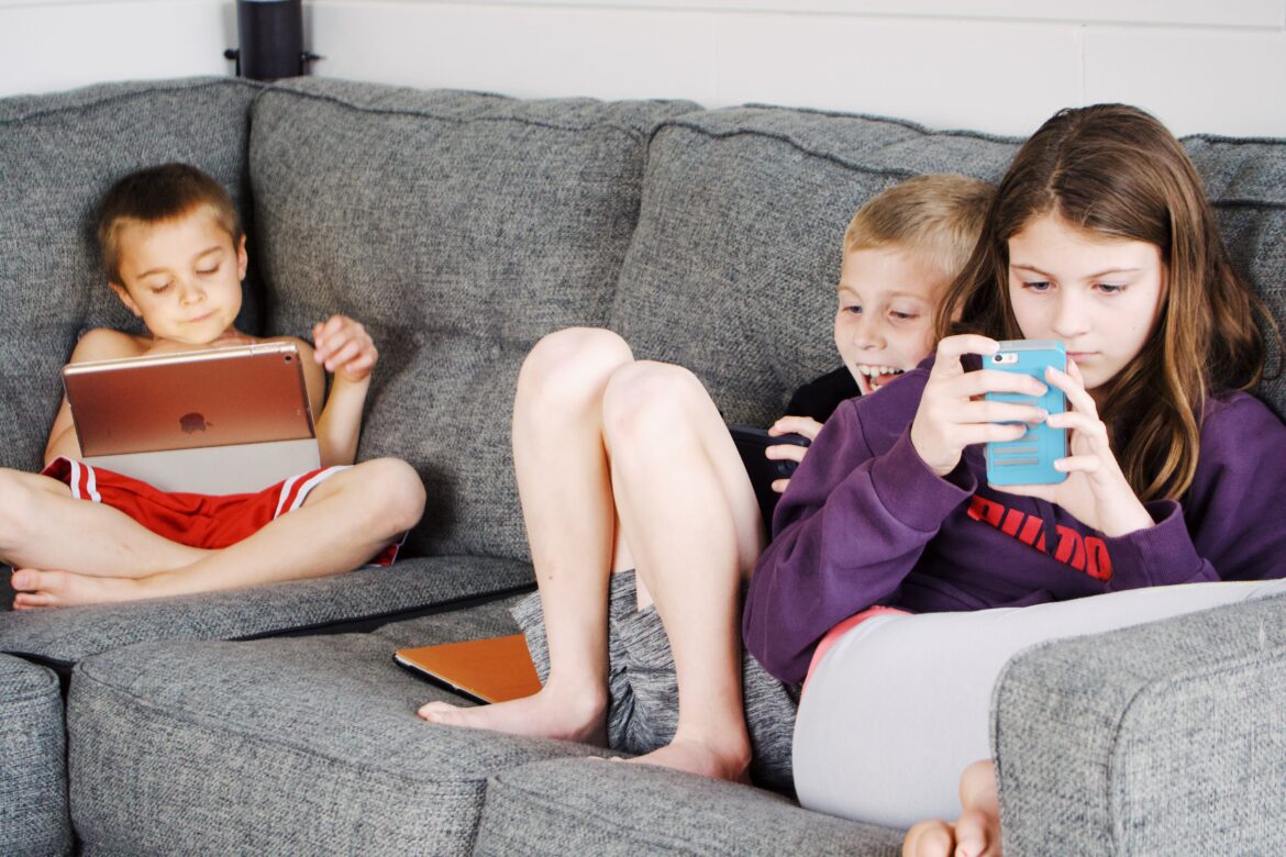 Barn sitter i soffan och tittar på mobilen och spelar med datorn.